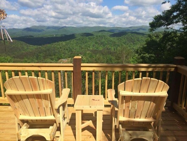 Une terrasse en bois avec deux fauteuils Adirondack et une petite table, offrant une vue sur un paysage montagneux.