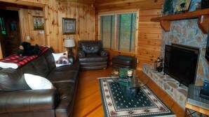 A cozy cabin interior with a leather sofa, a stone fireplace, and a ceiling fan. - Three Bears Bluff (Cherry Log)