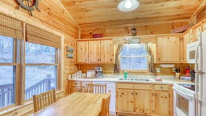 A cabin with wooden interior, a dining table, chairs, a kitchen with a sink, stove, and refrigerator. - The Bella Rose Retreat (Blue Ridge)