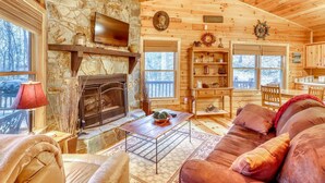 A cozy cabin interior with a stone fireplace, wooden walls, a television, and a comfortable seating area. - The Bella Rose Retreat (Blue Ridge)