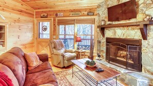 A cozy cabin interior with a stone fireplace, a leather sofa, a recliner, and a TV mounted on the wall. - The Bella Rose Retreat (Blue Ridge)