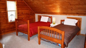 A cozy attic bedroom with two wooden beds, a small window with a birdcage, and a lamp on a nightstand.