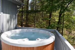 A hot tub on a wooden deck with a view of a forested area.