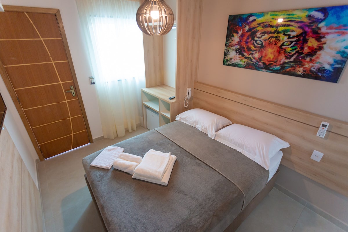 A neatly made bed with white linens, a wooden headboard, and a painting of a tiger on the wall.