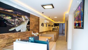 A modern hotel lobby with a reception desk, seating areas, and artwork on the walls. - Pousada Nascer do Sol (Arraial do Cabo)