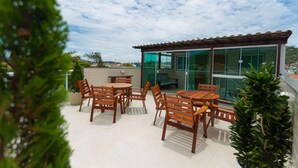 A patio with wooden furniture and potted plants, a glass wall, and a tiled floor. - Pousada Nascer do Sol (Arraial do Cabo)