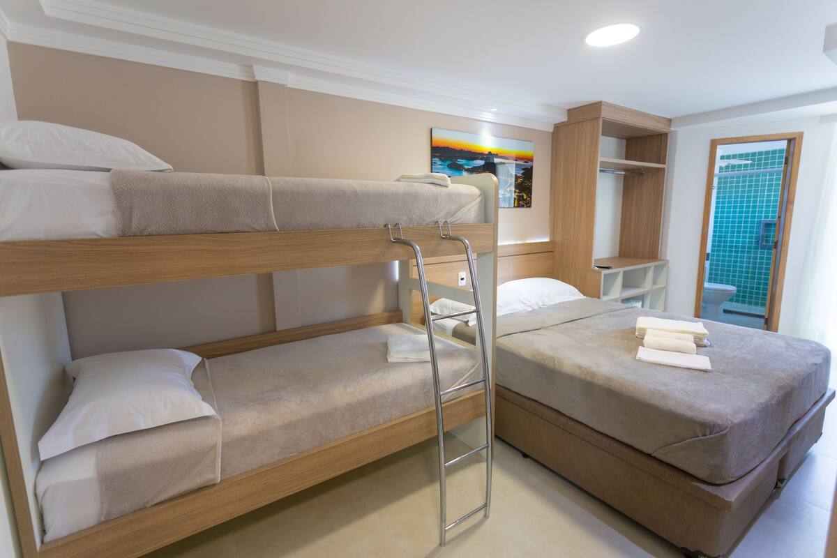 A bunk bed room with a ladder, a small shelf, and a bathroom with a tiled wall.