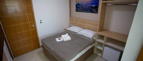 A bedroom with a bed, a small desk, a wardrobe, and a painting on the wall.