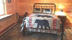 Quarto de cabana de madeira com cama e roupa de cama com tema de ursos.