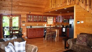 Interior de cabana de tronco com área de jantar, cozinha e escada.