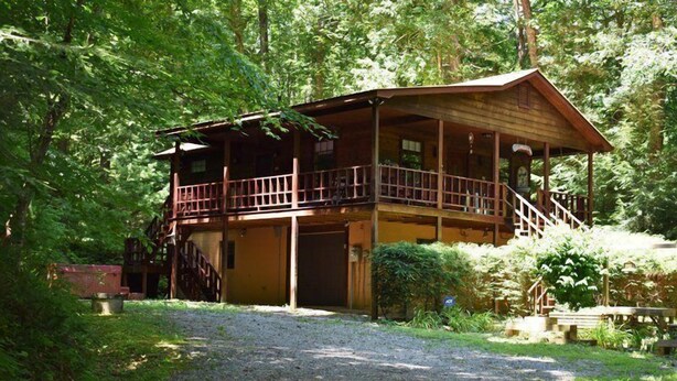 Een houten chalet met twee verdiepingen en een balkon, omgeven door een dicht bos.