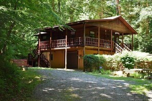 A two-story wooden cabin with a balcony, surrounded by dense forest. - Chattahoochee Chillin (Suches)