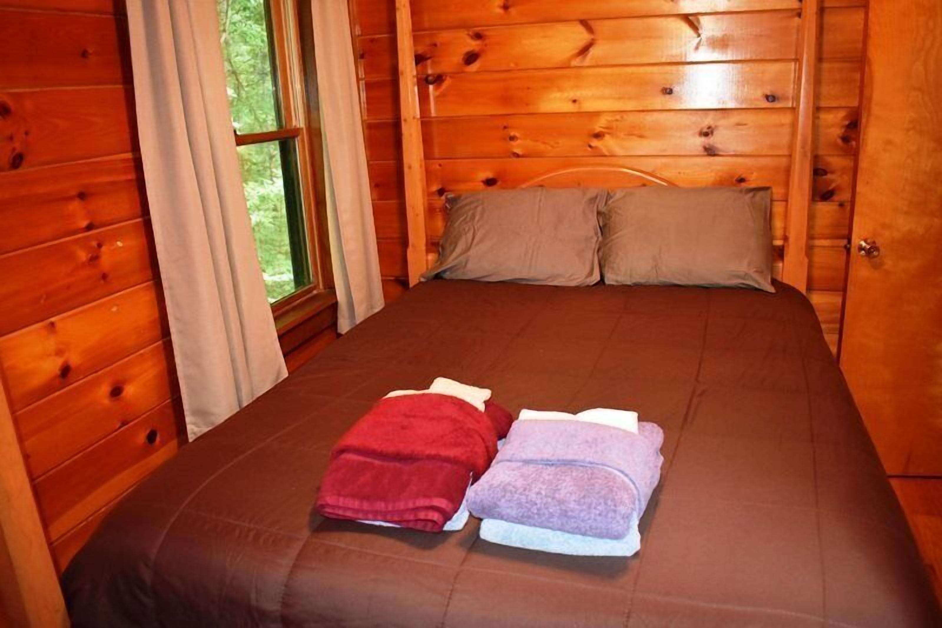A wooden cabin bedroom with a bed, two pillows, and a window.