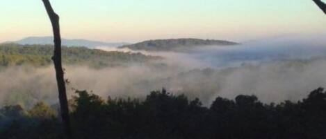 A view of a forested landscape with a misty valley and distant hills.