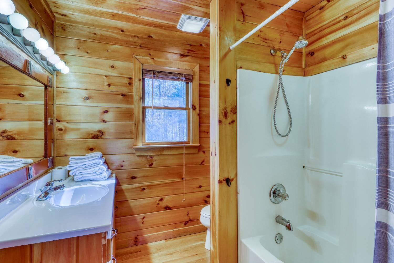 Baño de cabaña de madera con lavamanos, espejo y ducha.