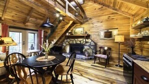 A cozy cabin interior with a stone fireplace, wooden beams, a dining area, and a kitchen. - Acorn Bungalow (Blue Ridge)