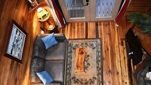 A cozy room with a wooden floor, a leather sofa with cushions, a decorative rug, and a small table with a lamp. - Acorn Bungalow (Blue Ridge)