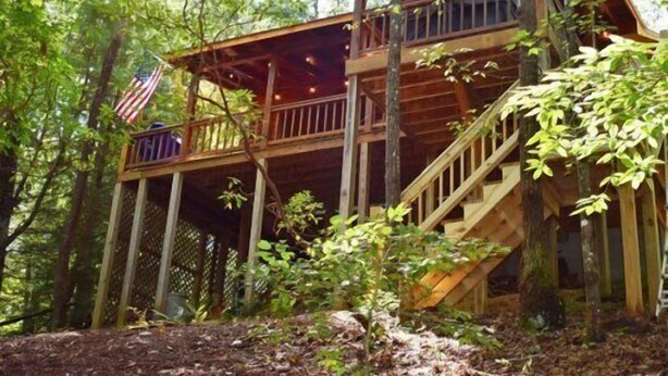 Una cabaña de madera con balcón y escalera, rodeada de árboles.