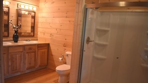Une salle de bain avec un lambris en bois, un lavabo avec un miroir, des toilettes et une douche à parois de verre.