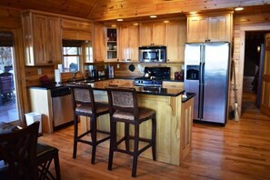 A wooden cabin interior with a kitchen featuring a central island, bar stools, a refrigerator, and a microwave. - Longview (Blue Ridge)