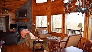 A cozy cabin interior with a fireplace, wooden walls, a dining area, and large windows. - Longview (Blue Ridge)