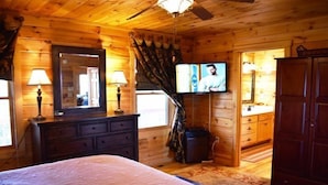 A wooden cabin bedroom with a bed, dresser, TV, and cabinets. - Longview (Blue Ridge)