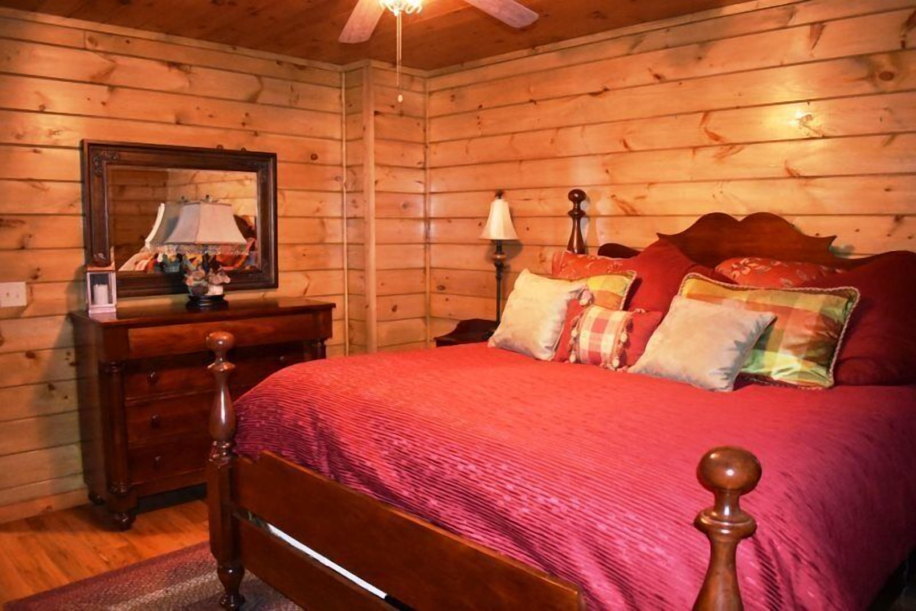Une chambre à coucher aux murs lambrissés, comprenant un lit, une commode, un miroir et un ventilateur de plafond.