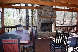 A covered outdoor seating area with a stone fireplace, surrounded by wooden furniture and a view of the forest. - Longview (Blue Ridge)
