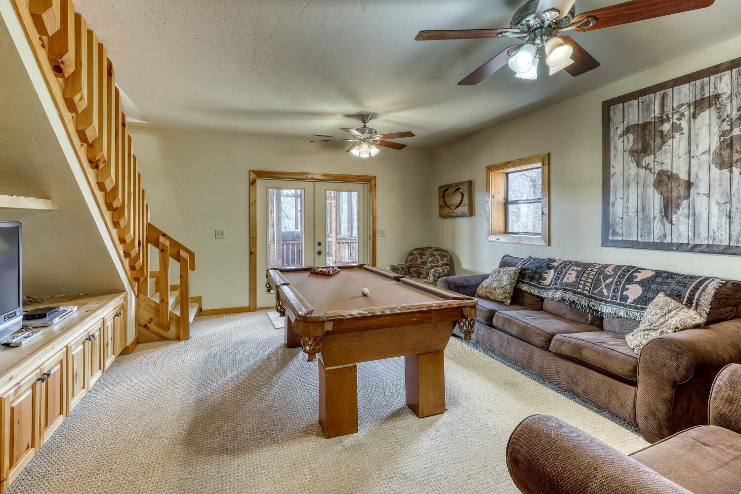 A cozy living room with a pool table, a sofa, a television, and a ceiling fan.