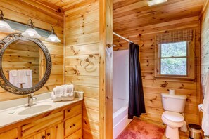 A wooden cabin bathroom with a vanity, sink, mirror, towel rack, shower curtain, toilet, and window. - Under The Stars (Blue Ridge)