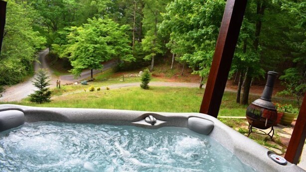 Un jacuzzi con vistas a un área boscosa y una parrilla de barbacoa al fondo.