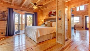 Un dormitorio de cabaña de madera con una cama, un ventilador de techo y un ventanal grande.