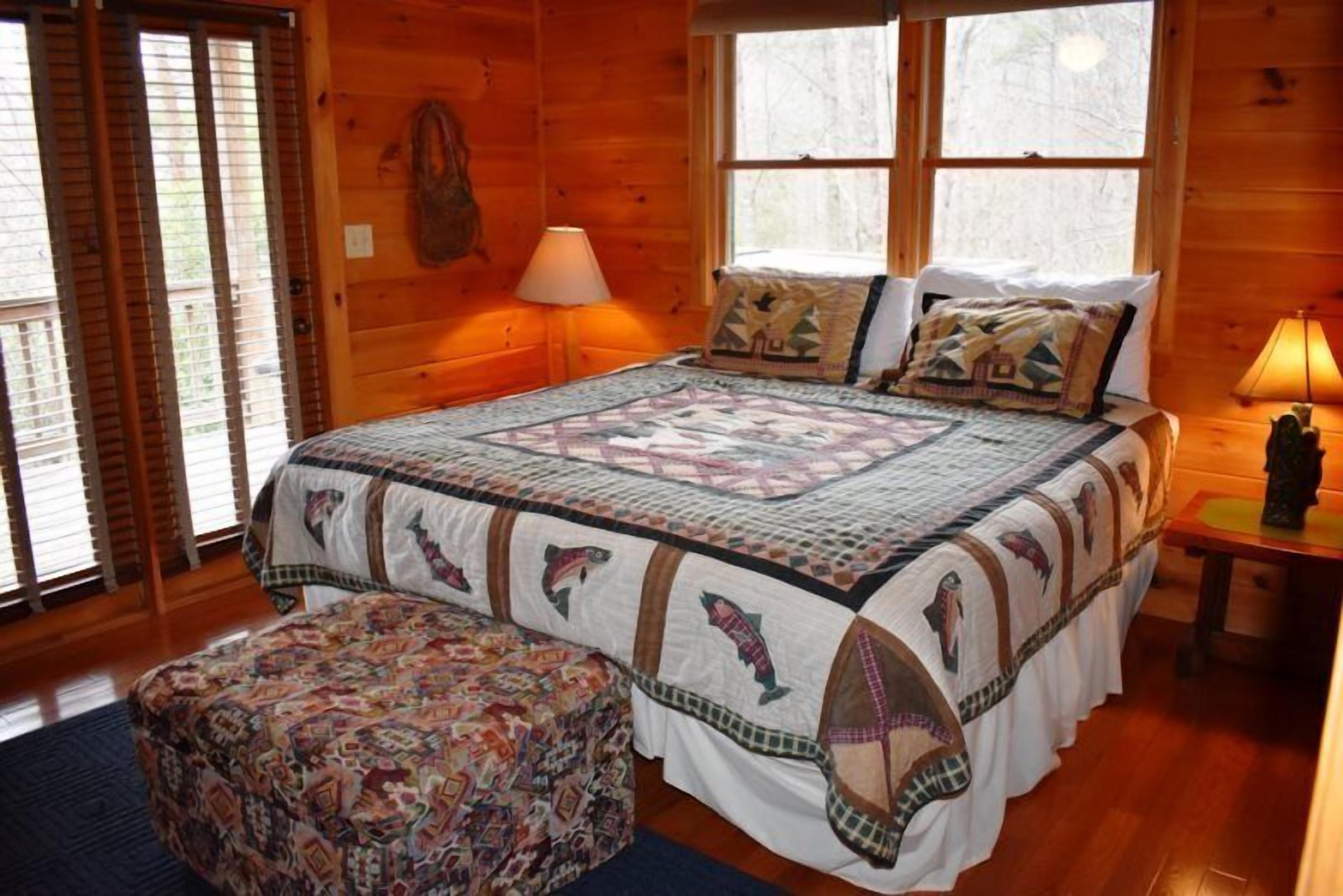 A wooden cabin bedroom with a large bed, a quilt, and a bench.
