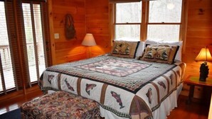 A wooden cabin bedroom with a large bed, a quilt, and a bench. - Serenity (Blue Ridge)