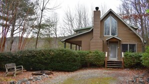 A log cabin with a front porch, a chimney, and a small front yard with a bench and rocks. - Serenity (Blue Ridge)