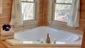 A wooden cabin with a large bathtub, two windows with curtains, and a pair of towels on a shelf. - Serenity (Blue Ridge)