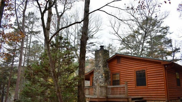 A log cabin with a stone chimney, surrounded by trees and a wooden deck. - Misty Lake Lodge (Blue Ridge)