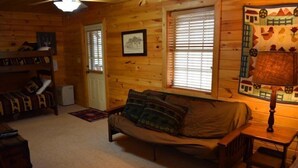 A cozy cabin interior with a sofa, a bookshelf, and a window with blinds. - Misty Lake Lodge (Blue Ridge)
