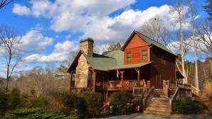 Une cabane en rondins avec une cheminée en pierre, une véranda en bois et une allée gravillonnée.