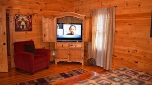 L’intérieur d’un chalet en bois, avec un téléviseur, un fauteuil rouge, un meuble et un tapis à motifs.
