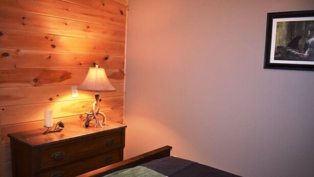 A wooden dresser with a lamp, a bed with a quilt, and a framed picture on the wall. - Wolf Mountain Hideaway (Mineral Bluff)
