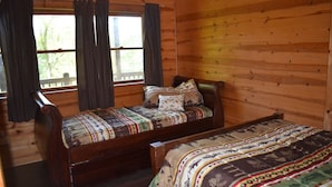 A cabin with two wooden beds, a window with curtains, and a wooden floor.