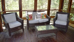 A covered porch with wicker furniture and a glass table.
