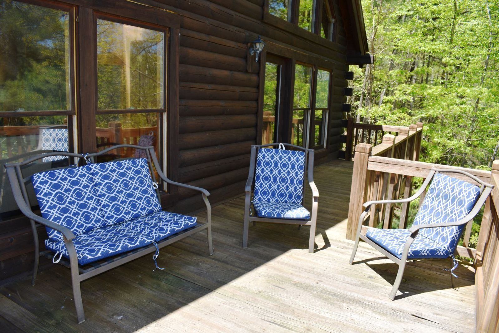 A wooden deck with three chairs and a sofa, all with blue patterned cushions.