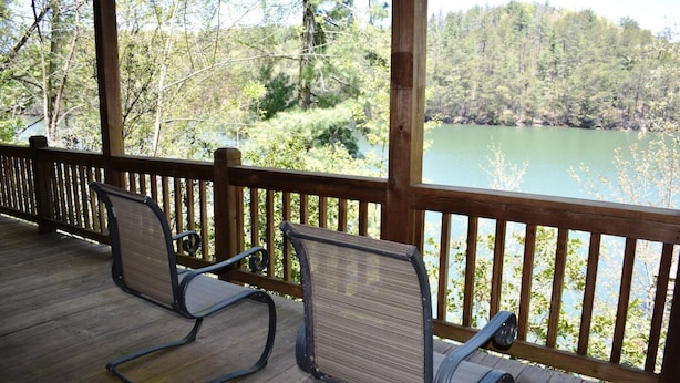 A wooden deck with two chairs facing a lake, surrounded by trees.