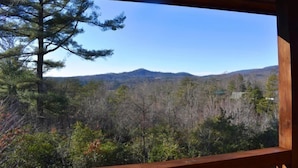 Vista desde un balcón de madera con vista a un paisaje boscoso y montañas a lo lejos.