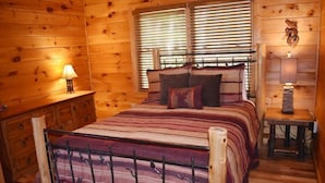 Un dormitorio de cabaña de madera con cama, dos mesitas de noche y una ventana con persianas.