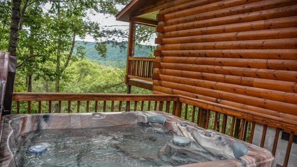Ein Whirlpool auf einer Holzterrasse mit Blick auf einen bewaldeten Gebirgszug.