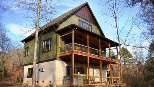Une maison en bois à deux étages, dotée d’un balcon et entourée d’arbres.