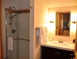 A bathroom with a glass-enclosed shower, a white sink, a mirror, and a towel rack.